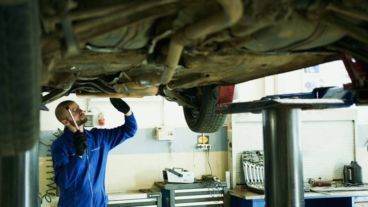 MOT tester inspecting a car on a lift in a garage